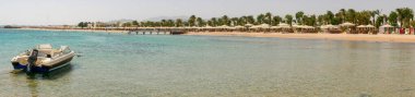 Hurghada, Mısır - 22 Eylül 2021: Motorlu tekneden ve Kızıl Deniz kıyısından panoramik manzara. İnsanlar dinleniyor, kumlu sahilde şemsiyeler ve güneş panelleriyle yüzüyor..