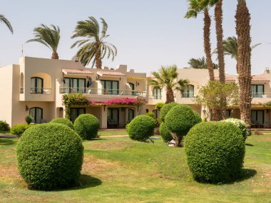 Hurghada, Mısır - 22 Eylül 2021: Evleri, yüksek palmiyeleri ve çimenlerinde yeşil yuvarlak çalıları olan güzel otel manzarası.