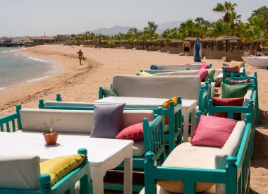 Hurghada, Mısır - 22 Eylül 2021: Kızıl Deniz kıyısındaki sahil barı. Çok renkli yastıklı kanepeler kumun üzerinde otururlar. Şemsiyeler ve yeşil palmiyeler..