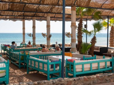 Hurghada, Mısır - 22 Eylül 2021: Kızıl Deniz kıyısındaki sahil barı. İnsanlar masalarda yastıklarla kanepelerde oturup konuşuyorlar..