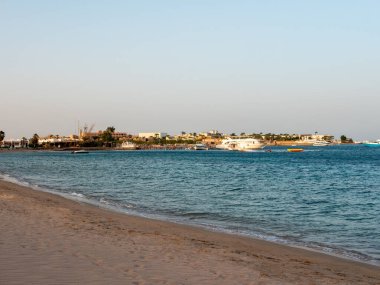 Hurghada, Mısır - 22 Eylül 2021: Kızıl Deniz 'in kumlu sahili gün batımında. Rıhtımın yanında yatlar ve tekneler duruyor, turistler deniz gezisinden dönüyorlar. Boşluğu kopyala.