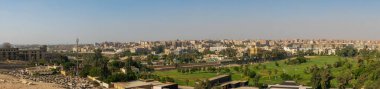 Giza, Kahire, Mısır - 30 Eylül 2021 Kahire 'nin panoramik manzarası. Şehir binalarının arka planında yeşil çimenli ve uzun palmiye ağaçları olan park.
