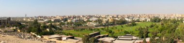 Giza, Kahire, Mısır - 30 Eylül 2021 Kahire 'nin panoramik manzarası. Şehir binalarının ve gökyüzünün zeminine karşı yeşil çimenli ve uzun palmiye ağaçları olan park.