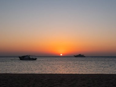 Hurghada, Mısır - 3 Ekim 2021: Mısır 'da Kızıldeniz' de güzel bir gün doğumu. Yatlar, ufukta yükselen parlak güneşin arka planına karşı denizde duruyor..