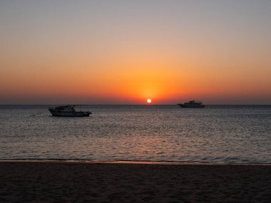 Hurghada, Mısır - 3 Ekim 2021: Mısır 'da Kızıldeniz' de güzel bir gün doğumu. Ufukta yükselen güneşin arka planına karşı iki yat denizde duruyor..