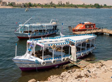 Luxor, Mısır - 3 Ekim 2021: Nil Nehri manzarası ve Luxor kıyıları. Turistlerin binmesi için kıyıya yakın tekneler duruyor.