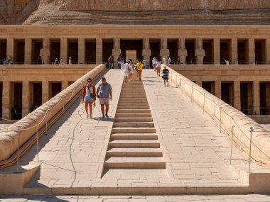 Luxor, Mısır - 3 Ekim 2021: Mısır dağlarındaki Kraliçe Hatshepsut tapınağının ana girişine bakın. İnsanlar tapınağa taş bir merdivenden giriyor..