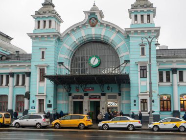Moskova, Rusya - 5 Ekim 2021 Belorussky tren istasyonu. İnsanlar binanın girişinin yanında duruyorlar. Taksi arabaları yol kenarında bir sıraya park edilmiş..