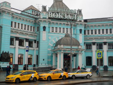 Moskova, Rusya - 5 Ekim 2021 Belorussky tren istasyonu, ana giriş. İnsanlar binanın girişinde dikiliyorlar. Taksi arabaları yol kenarında sıra sıra bekliyor..