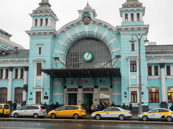 Moskova, Rusya - 5 Ekim 2021 Belorussky tren istasyonu. İnsanlar binanın girişinin yanında duruyorlar. Taksi arabaları yol kenarında bir sıraya park edilmiş..