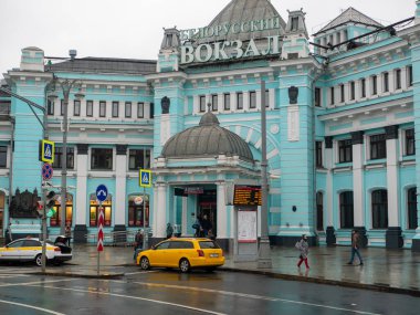 Moskova, Rusya - 5 Ekim 2021 Belorussky tren istasyonu, ana giriş. İnsanlar yağmurlu bir sonbahar gününde kaldırımda yürürler. Taksi arabaları yol kenarında sıra sıra bekliyor..