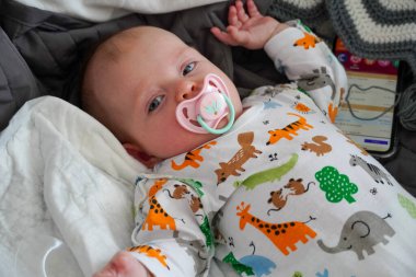 Ağzında emzik olan beyaz bir bebek sırt üstü yatarak rahatlıyor..