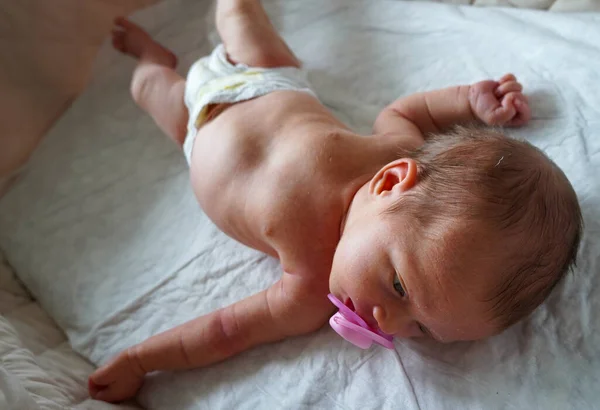 Naked baby caucasian child with a pacifier in his mouth relaxes lying his back. — Stockfoto