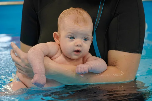 A small baby child swims in the pool for the first time. With a coach. 免版税图库图片