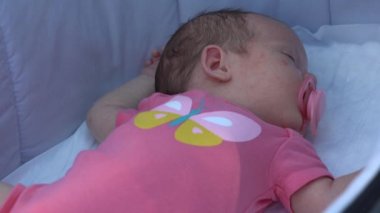 Ağzında emzik olan beyaz bir bebek sırt üstü yatarak rahatlıyor..
