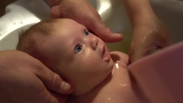 Een pasgeboren baby wordt gewassen in de badkamer. Er wordt water uit de pan overheen gegoten. — Stockvideo