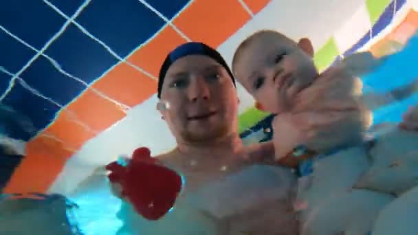 Un padre varón y un bebé recién nacido nadan en la piscina. Vista desde debajo del agua. — Vídeos de Stock