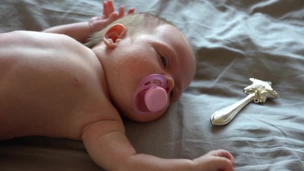 Huilend pasgeboren baby kind op een bed met een ijzeren zilveren rammelaar en een fopspeen — Stockvideo