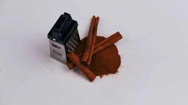 Beyaz arka planda izole edilmiş tarçın çubukları ve pudrası olan küçük bir rende.