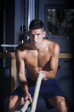 Muscular man in gym with battle ropes clipart