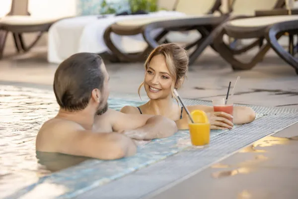 Attractive Young Couple Relaxing Indoor Hotel Swimming Pool Drinking Juice — Stock Photo, Image