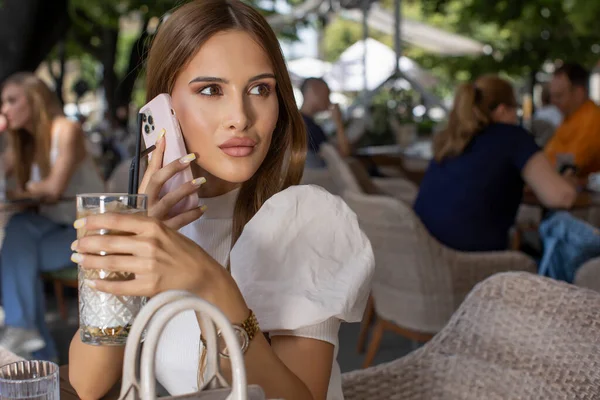 美丽的年轻女子在户外咖啡馆用智能手机交谈 — 图库照片