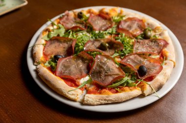 Arugula prosciutto pizza beyaz tabakta servis edilir.