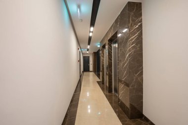 İçinde paslanmaz çelik asansör kapıları olan mermer bir koridor.