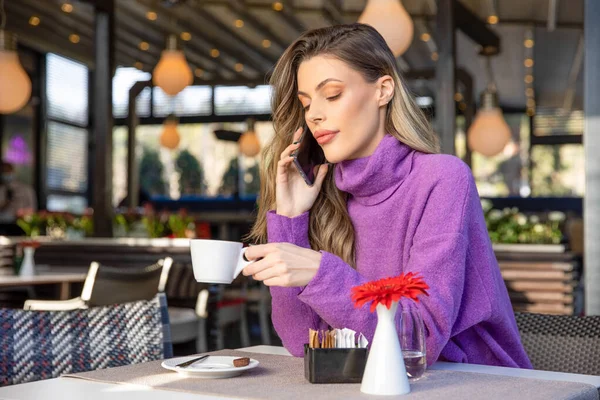 カフェバーでコーヒーを飲みながらスマホで話すゴージャス女性 — ストック写真
