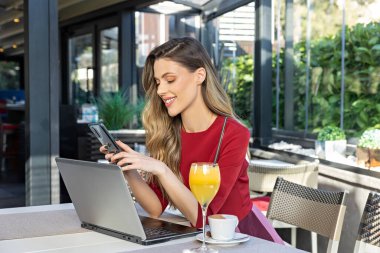 Kafe barında akıllı telefonunu kullanarak defter üzerinde çalışan güzel bir kadın.
