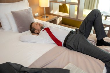Takım elbiseli bir iş adamı otel yatağında dinleniyor.