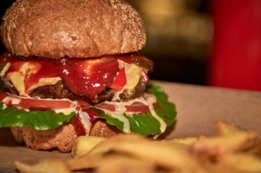 Lezzetli ızgara burger, biftek, peynir, pastırma ve sosla ahşap masada patates kızartması ve bira.