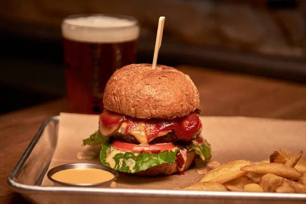 Lezzetli ızgara burger, biftek, peynir, pastırma ve sosla ahşap masada patates kızartması ve bira.