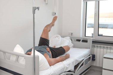 Hastane koğuşunda yatağında kateter takmış bir adam var. Elastik omuz kırığı. Acil durum.