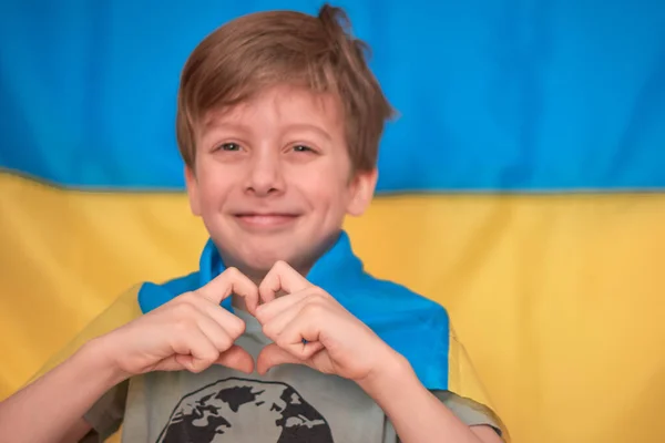Chłopiec trzyma w rękach ukraińską żółto-niebieską flagę. Dzieci wspierają Ukrainę pokazując serce — Zdjęcie stockowe