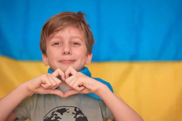 Chłopiec trzyma w rękach ukraińską żółto-niebieską flagę. Dzieci wspierają Ukrainę pokazując serce — Zdjęcie stockowe