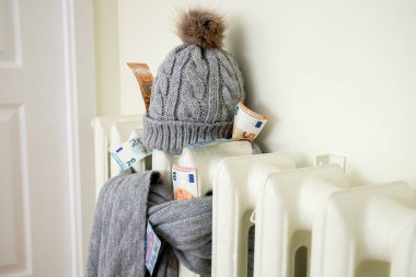 Vintage heating radiator with winter hat and scarf stuffed with euro money. The electricity bill goes up, European energy crisis concept.  clipart