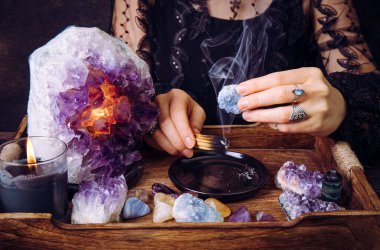 Siyah elbiseli çekici kadın Palo Santo 'nun tahta çubuğunu kirleterek kristalleri temizliyor. Negatif enerjiyi kaldır.