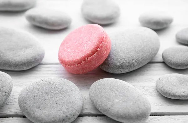 Pink color solid shampoo, conditioner bar on flat sea stones. Minimalist beauty set indoors. Shallow depth of field.