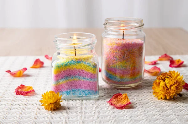 Children made fun colorful layered wax powder candles in home by pouring powder in old baby food jar and inserting wick inside, minimal background. Hobby concept.