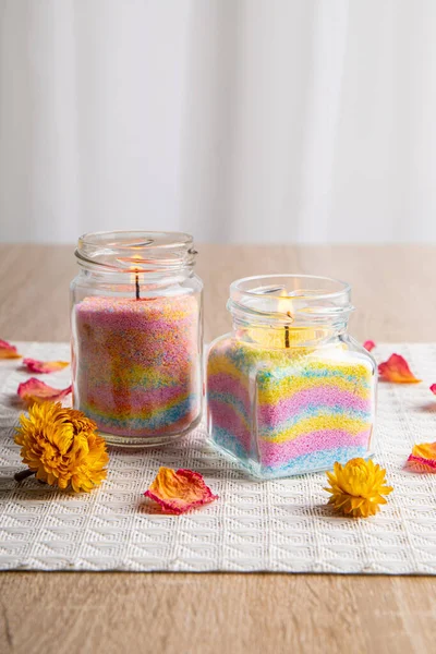 Children made fun colorful layered wax powder candles in home by pouring powder in old baby food jar and inserting wick inside, minimal background. Hobby concept.