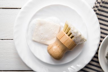 Köpükle kaplı katı bulaşık deterjanı. Sıfır israf yaşam tarzı. Bulaşık deterjanı ve köpüklü mutfak temizleme sisal bambu yuvarlak bulaşık fırçası. Minimalist beyaz tahta arkaplan. 
