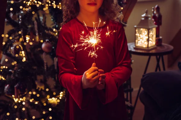 家のリビングルームで手に輝くキャンドルを保持するかわいい女の子の子供は 背景にクリスマスツリーを飾られ 暗い部屋は 輝くキャンドルによって照らされました 明けましておめでとうございます — ストック写真