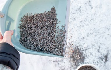 Kaygan yollarda kullanılan çakıllar. Kayganlığı azaltmak için yaya yoluna çakıl kumu saçan biri. Patinaj bakım çalışması.