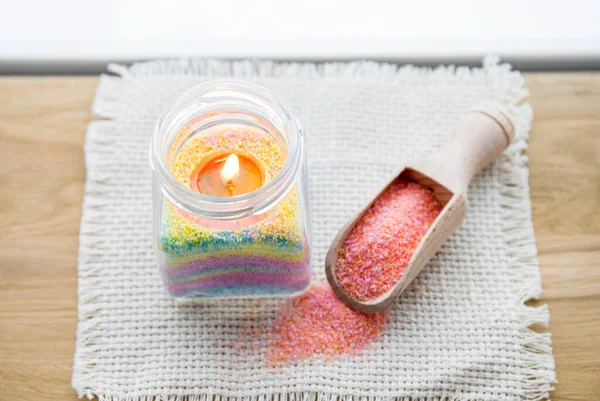 Child made fun colorful layered wax powder candle in home by pouring powder in old baby food jar and inserting wick inside, minimal background. Hobby concept.