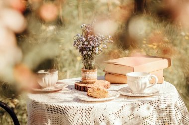 Elma çiçeklerinden masaya çay fincanları ve kitaplarla kurulmuş bir hayal gibi düşün. Bir buket kır çiçeği Unutun beni el yapımı kavanoz vazosunda..