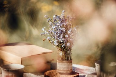 Elma çiçeklerinden masaya çay fincanları ve kitaplarla kurulmuş bir hayal gibi düşün. Bir buket kır çiçeği Unutun beni el yapımı kavanoz vazosunda..