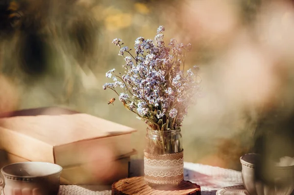Elma çiçeklerinden masaya çay fincanları ve kitaplarla kurulmuş bir hayal gibi düşün. Bir buket kır çiçeği Unutun beni el yapımı kavanoz vazosunda..