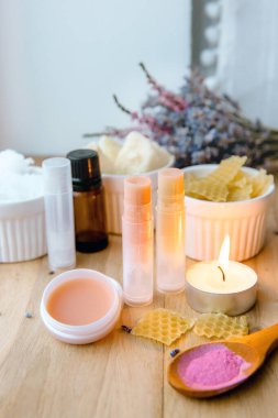  Ev yapımı dudak kremi: Shea yağı, gerekli yağ, mineral rengi pudrası, balmumu, hindistan cevizi yağı. Ev yapımı dudak kremi karışımı ve etrafa saçılmış malzemeler..