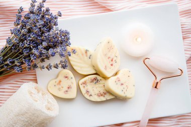 Küçük kalp ve yaprak şekilli banyo mantarları, banyo bombasının tereyağlı versiyonu beyaz tepside mum yakma ve gül kuvars suratlı yuvarlama aleti. Ev spa konsepti.